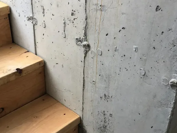 Unfinished basement wall inspection showing crack and form tie holes